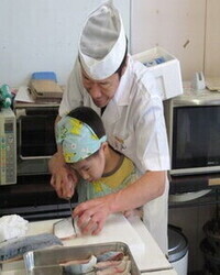 子供が講師と一緒に魚を切る写真
